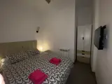 Interior apartment bedroom seen from the doorway with ceiling fan, pink towels on the bed and wardrobe beyond